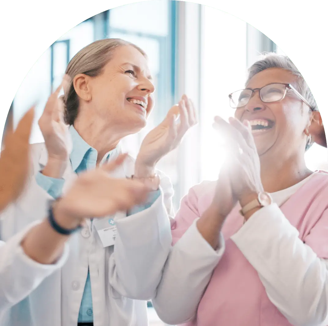 2.0About-min Three people, including a doctor in a lab coat, laughing and clapping.